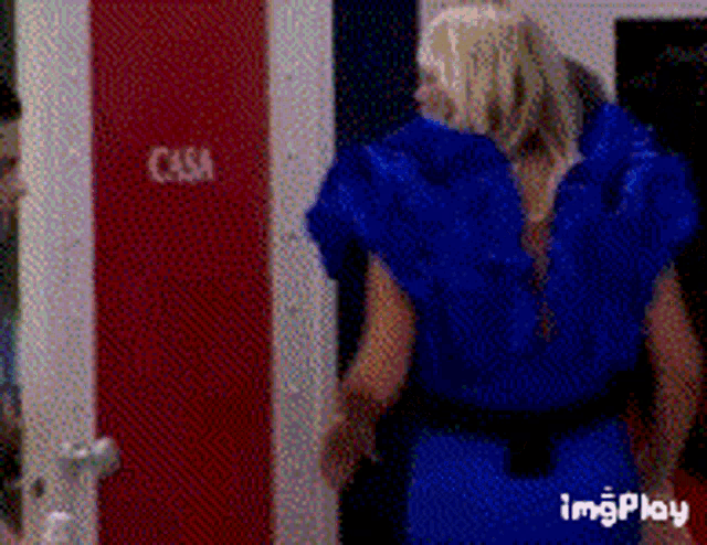 a woman in a blue dress is standing in front of a red door that says casa .