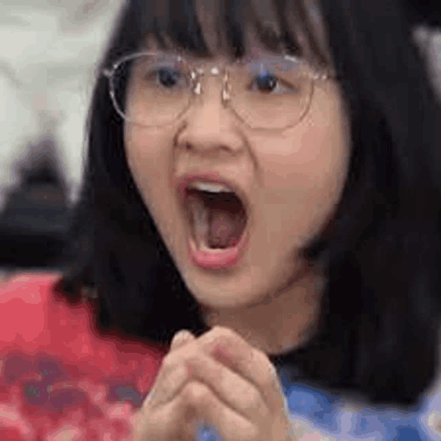 a close up of a girl wearing glasses with her mouth open .