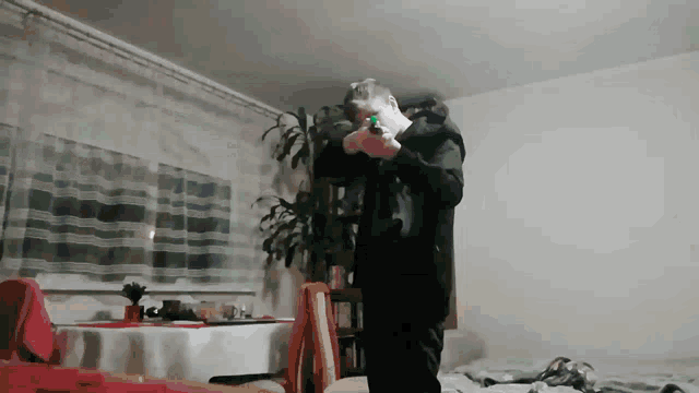 a man holding a gun in a living room with a plant in the background