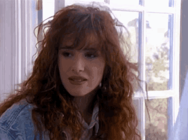 a woman with red hair and bangs is looking out a window