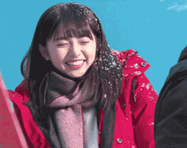 a woman wearing a scarf and a red jacket is smiling in the snow