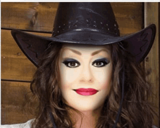 a woman wearing a black cowboy hat with a fake face on her face