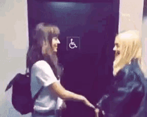 two women are holding hands in front of a handicapped sign .