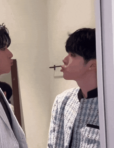 a man with a cigarette in his mouth looks at another man in front of a mirror