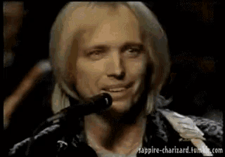 a man with blonde hair is singing into a microphone and smiling
