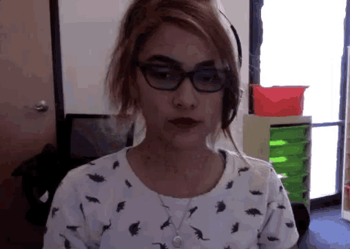 a woman wearing glasses and a dinosaur shirt is looking at the camera