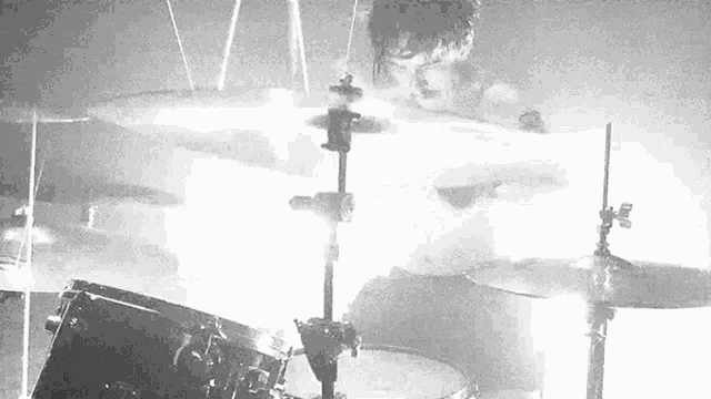 a black and white photo of a man playing drums in a dark room .