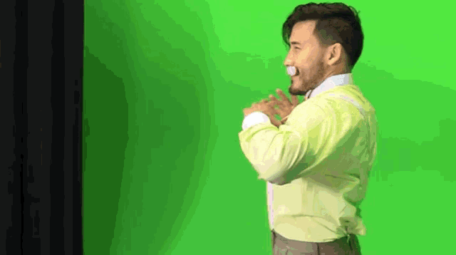 a man in a yellow shirt and suspenders is standing on a green screen .