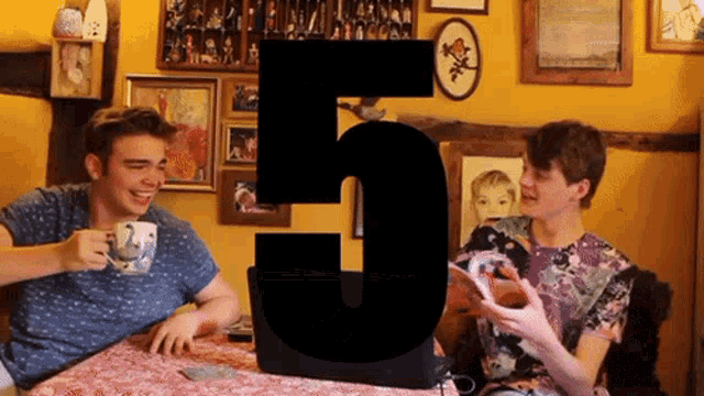two young men are sitting at a table with the number 5 in the corner