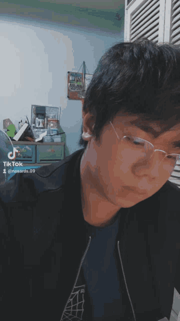 a young man wearing glasses and a black jacket has a tiktok icon on his face