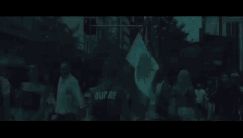 a man is holding a flag in front of a crowd of people on a city street .