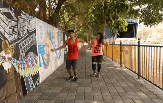 a man and a woman are dancing on a sidewalk in front of a wall that has graffiti on it