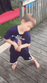 a young boy wearing a shirt that says all american is standing on a deck