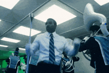 a man in a suit and tie is dancing in front of a band with the letter m on their back