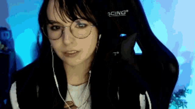 a woman wearing glasses and earbuds is sitting in a gaming chair .