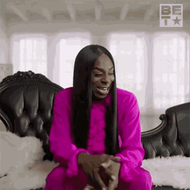 a woman with long hair is sitting on a couch wearing a pink dress .