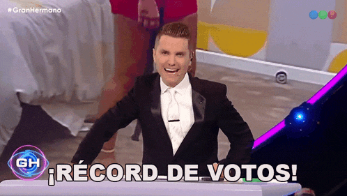 a man in a tuxedo is standing in front of a sign that says record de votos
