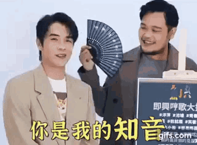 two men are standing next to each other and one is holding a fan in his hand .