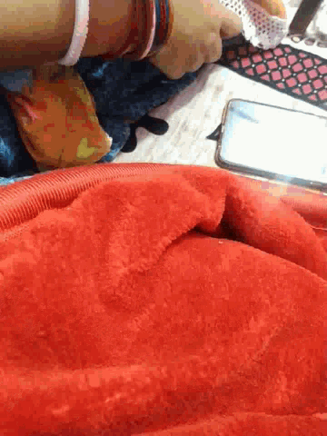 a person laying on a bed with a red blanket and a cellphone