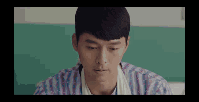 a man in a striped shirt is sitting in a hospital bed looking down .