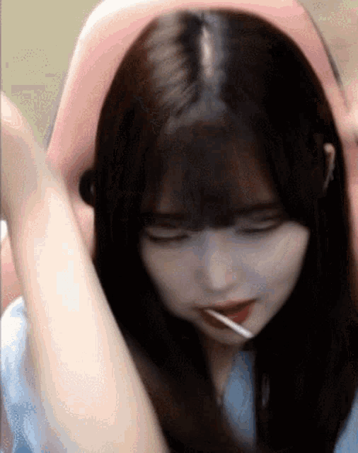 a girl with long hair is sitting in a pink chair with her eyes closed and a lollipop in her mouth .