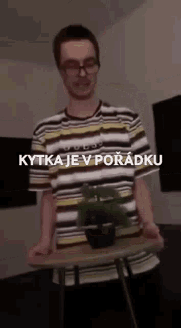 a man in a striped shirt is holding a potted plant on a table with the words kytka je v poradku on the bottom