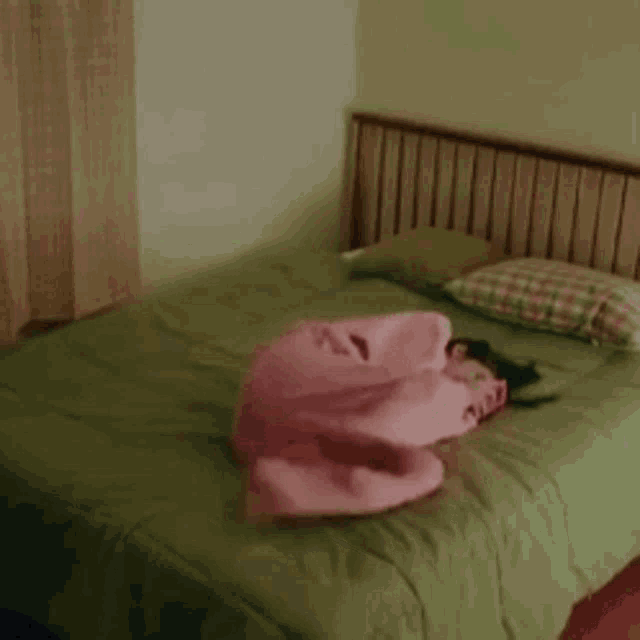 a woman in pink pajamas is laying on a bed with a green comforter .