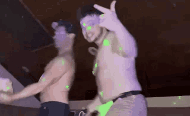 two shirtless men are dancing in a dark room with green lights on the ceiling .