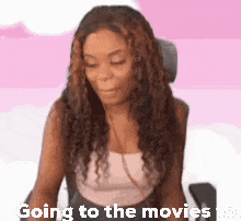 a woman with curly hair is sitting in a chair with the words `` going to the movies '' written on her face .