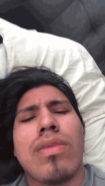 a man with long hair and a beard laying on a bed with his eyes closed