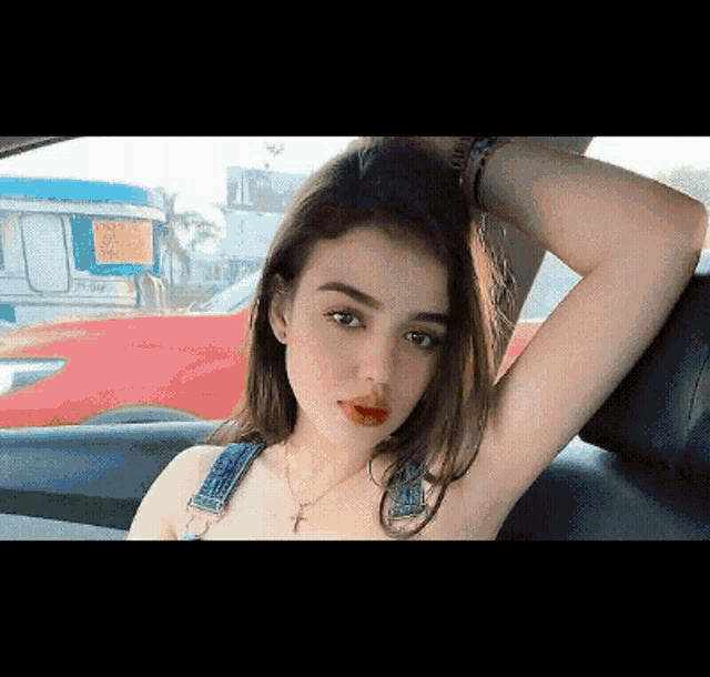 a young woman is sitting in a car with her arm over her head