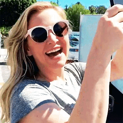 a woman wearing sunglasses and a grey shirt smiles