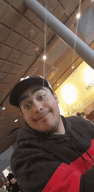 a man wearing a black hat and a red jacket is taking a selfie