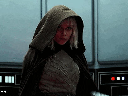 a woman in a cape with a hood is standing in front of a wall .