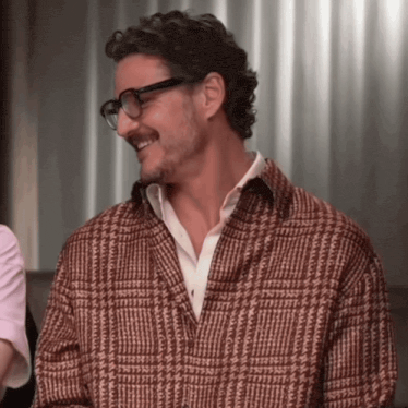 a man wearing glasses and a plaid shirt smiles for the camera
