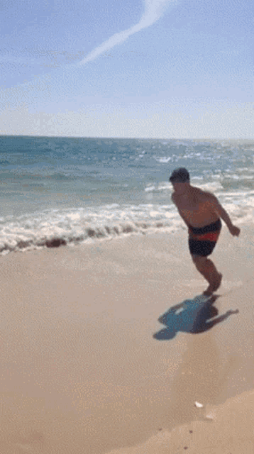 a shirtless man jumps in the air on a beach