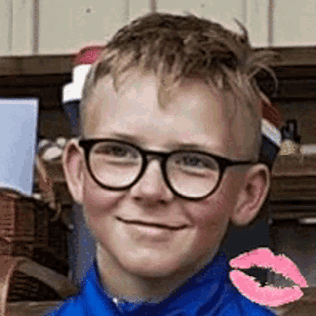 a young boy wearing glasses and a blue shirt is smiling with a pink kiss on his cheek .