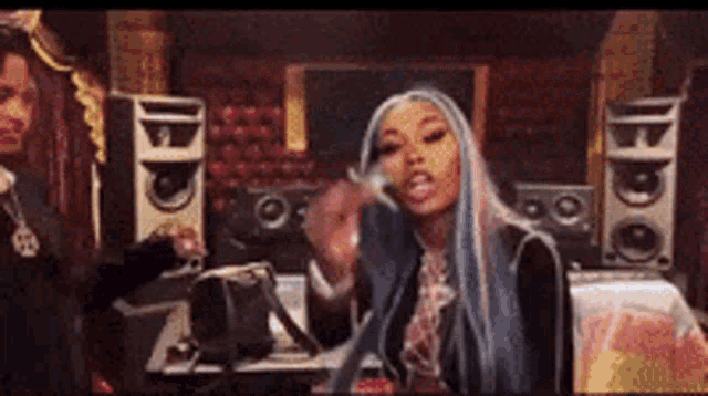 a woman with long blue hair is standing in front of a microphone in a room with speakers .