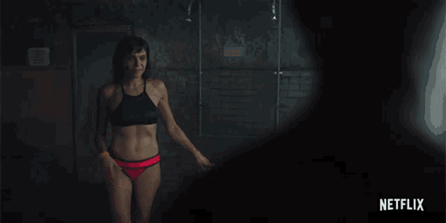 a woman in a black bra is standing next to a man in a dark room with netflix written in the corner