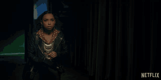 a woman in a leather jacket is standing in a dark room with a netflix logo in the corner