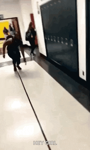 a woman is walking down a hallway in a school with the words `` hey girl '' written on the floor .