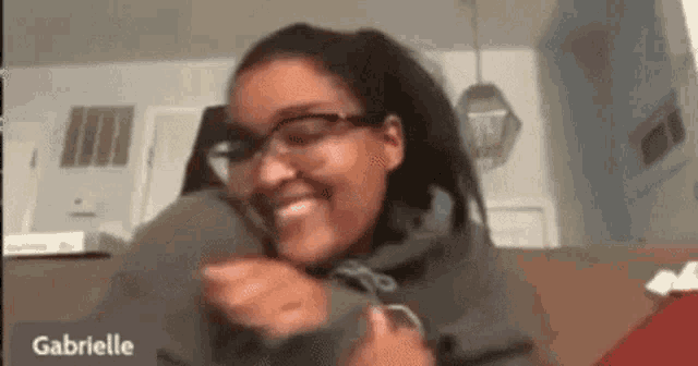 a woman wearing glasses is smiling while sitting on a couch in a living room .