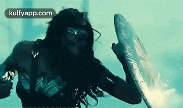 wonder woman is holding a shield in her hand and fighting a man in a pool .