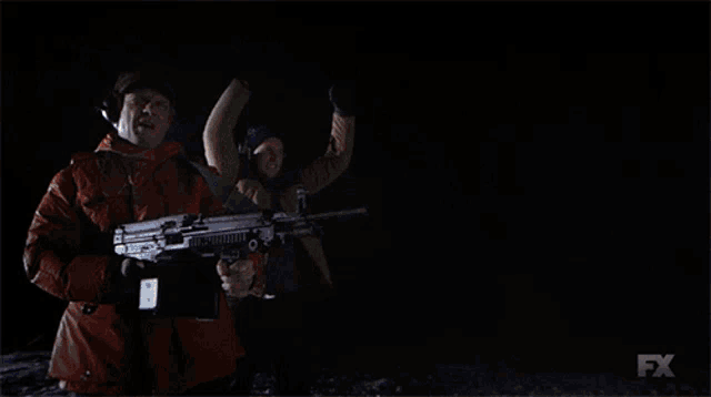 a man in an orange jacket is holding a machine gun with a fx logo in the background