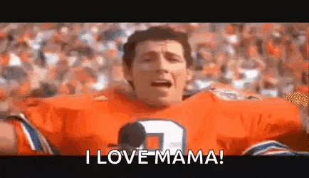 a man in an orange football jersey is saying `` i love mama '' in front of a crowd of people .