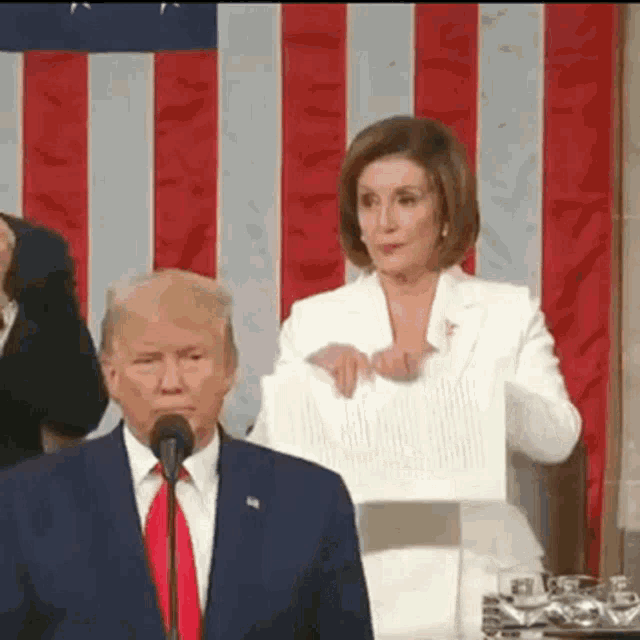 a man in a suit and tie is standing in front of a microphone while a woman holds a piece of paper .