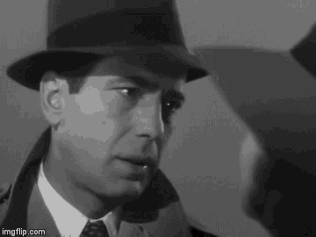 a man in a hat and tie is looking at another man in a suit .