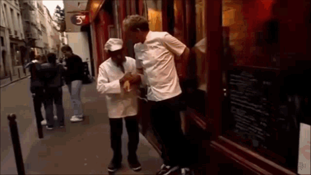 a man in a chef 's hat talks to another man in front of a restaurant with a sign that says 3 on it