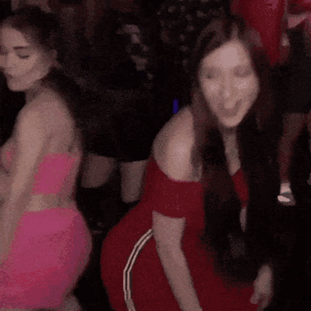 two women in pink and red dresses are dancing in a dark room
