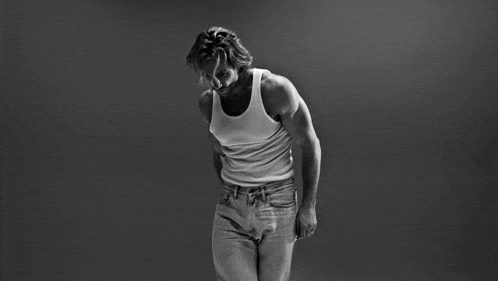 a black and white photo of a man in a tank top and jeans
